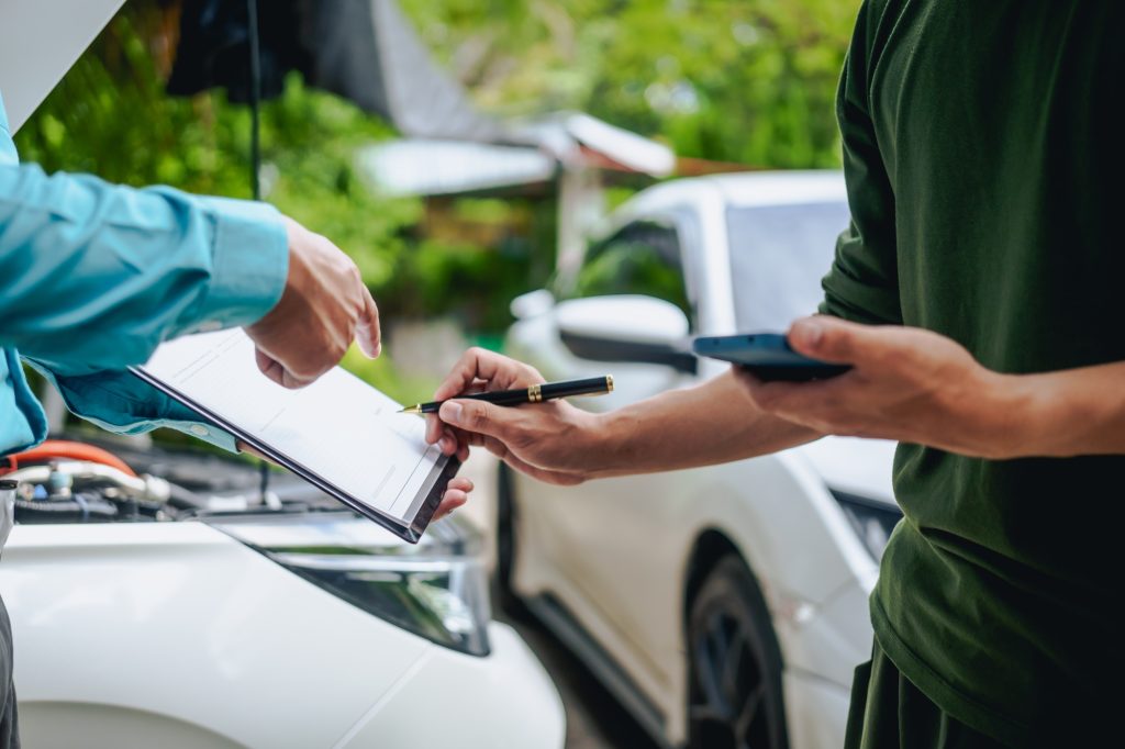 Asian clients engage with a car insurance agent beside a wrecked vehicle. examine policy details