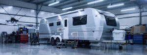a sleek, well-maintained caravan is parked in a modern workshop on the gold coast, showcasing its polished exterior under bright fluorescent lights, with various tools and equipment neatly arranged in the background to emphasise a rigorous roadworthy inspection process.